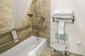 A bathroom with a bathtub, a shower with a handheld showerhead, a grab bar, a towel rack, and a small stool.