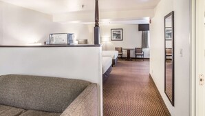 A hotel room with a large grey sofa, a bed, a desk with a computer, a chair, and a small table.