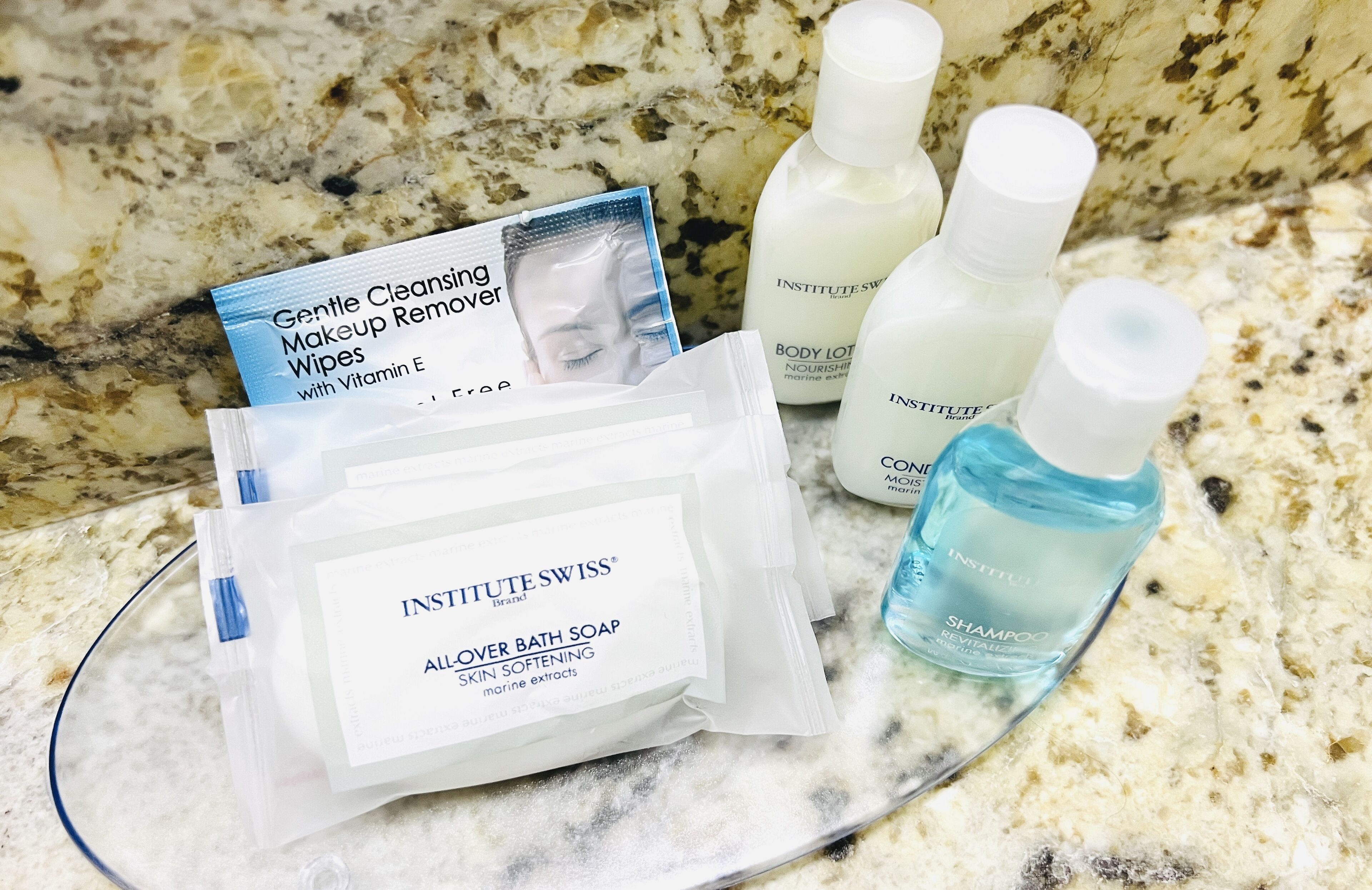 A bathroom counter with various skincare products including a makeup remover wipes package, body lotion, and a bottle of shampoo.