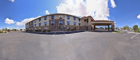 Un hotel de varios pisos con fachada curva, entrada cubierta y estacionamiento.