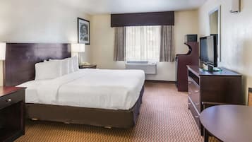 A hotel room with a large bed, a desk, a television, and an air conditioning unit.
