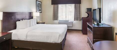 A hotel room with a large bed, a desk, a television, and an air conditioning unit.