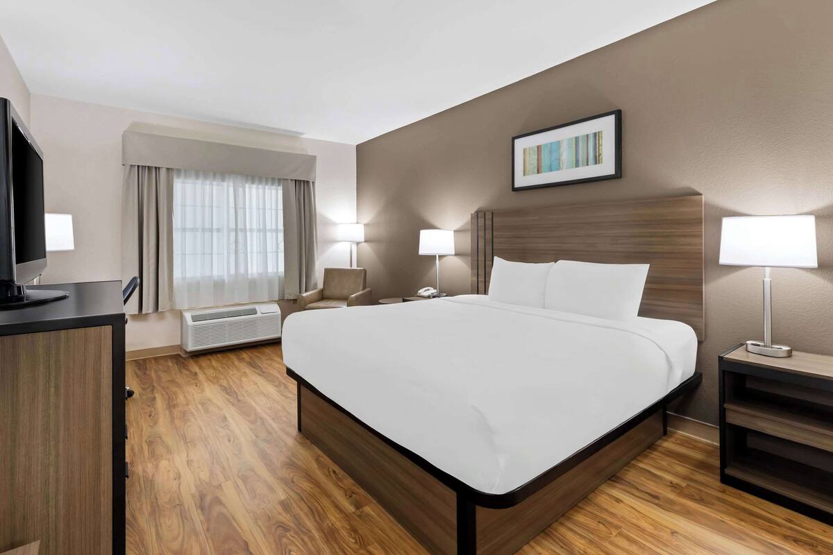 Una habitación de hotel con una cama grande, lámparas de noche, televisión, escritorio y ventana con cortinas.