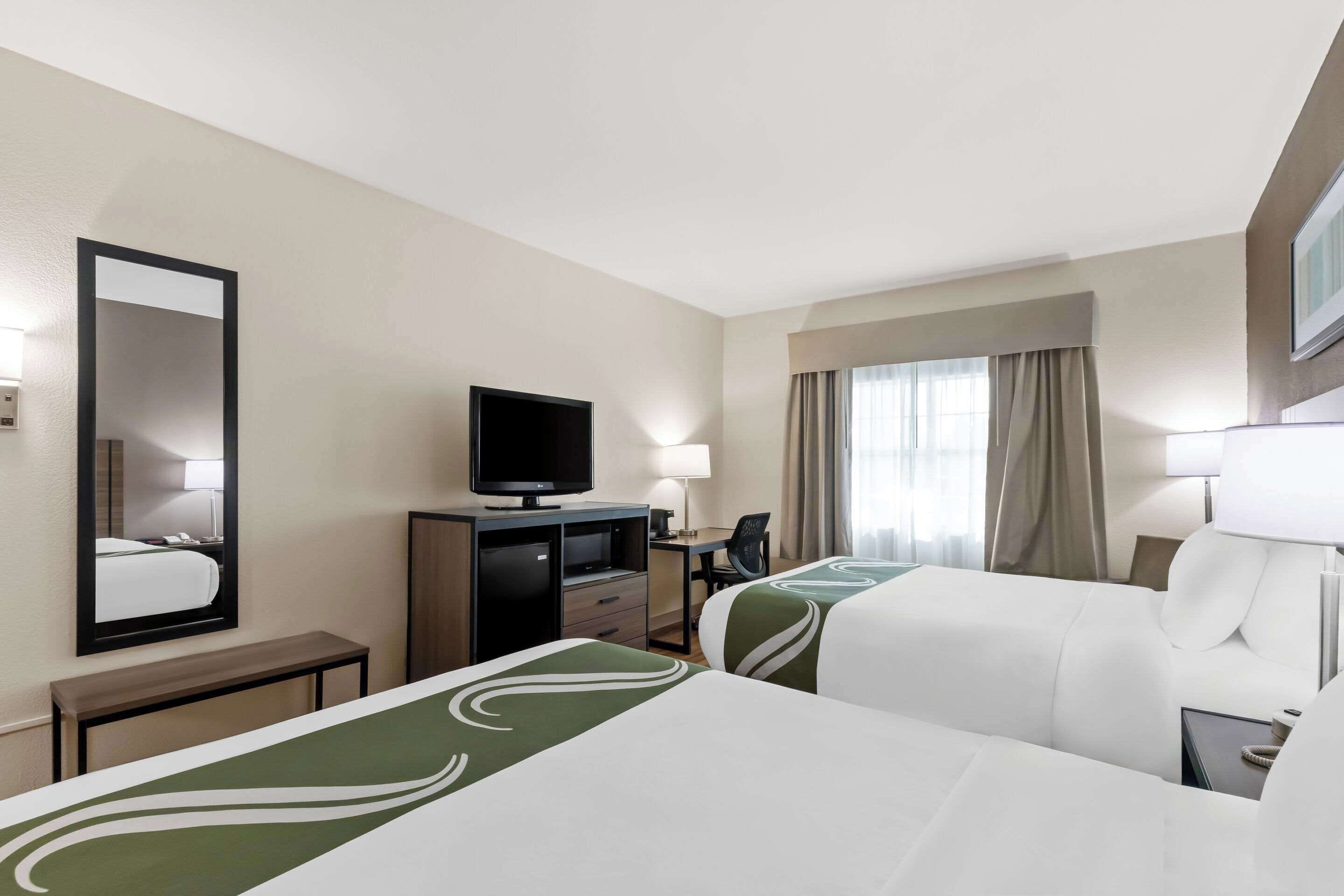 Une chambre d’hôtel avec deux lits, un bureau, une télévision et une fenêtre avec des rideaux.
