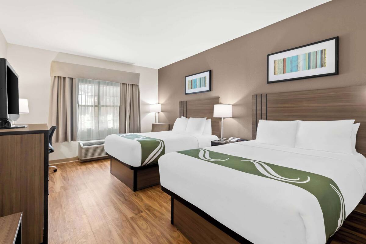 Habitación de hotel con dos camas, un escritorio, un televisor y una ventana con cortinas.