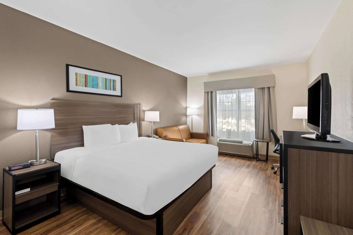 Habitación de hotel con una cama grande, dos mesitas de noche con lámparas, un televisor sobre un escritorio y una ventana con cortinas.