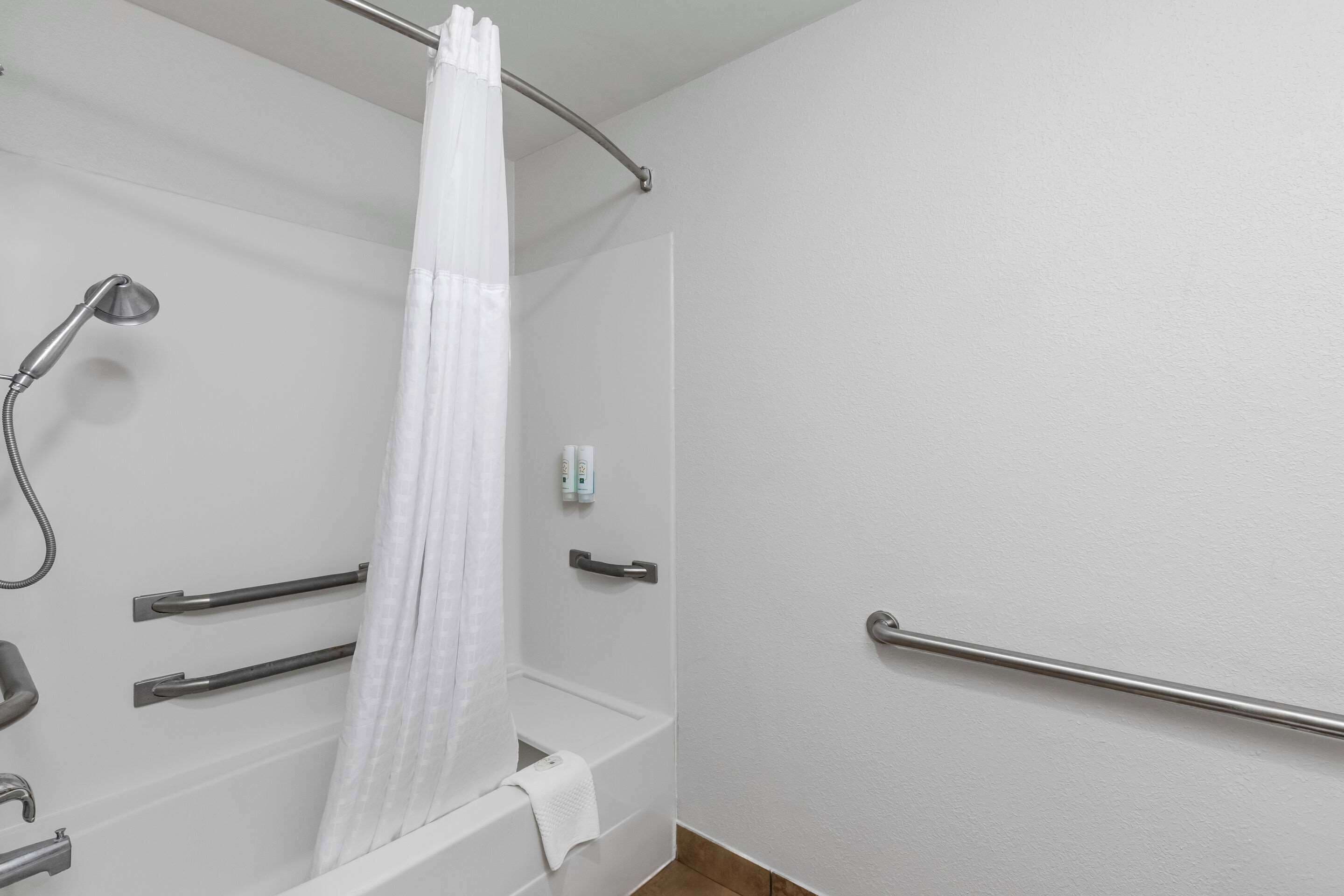 A bathroom with a shower, grab bars, a towel rack, and a toilet.