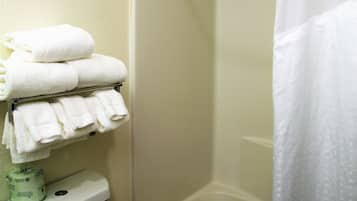 A bathroom with a toilet, a stack of white towels, a shower curtain, and a bathtub.