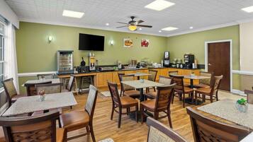 A restaurant with wooden tables and chairs, a kitchen area, and a ceiling fan.