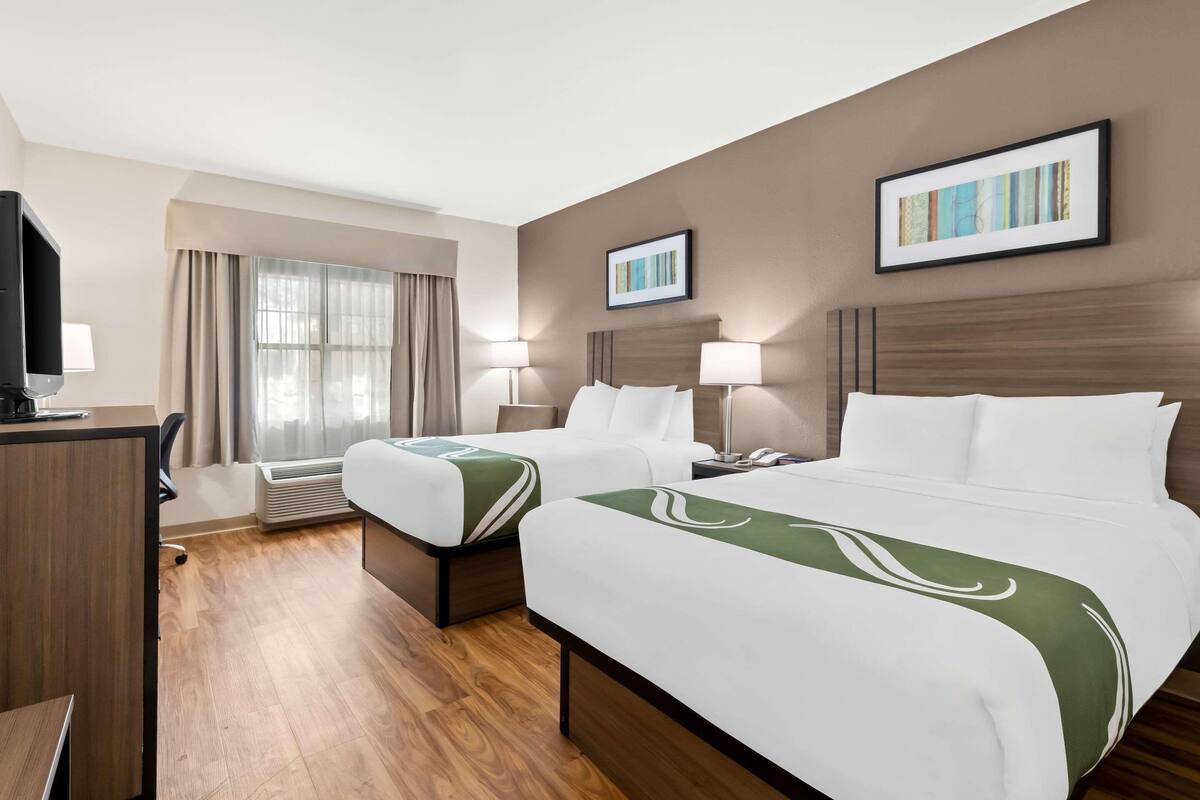 Una habitación de hotel con dos camas, un escritorio, un televisor y una ventana con cortinas.