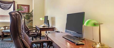 Habitación de hotel con escritorio de madera, computadora, dos sillas, lámpara y planta.