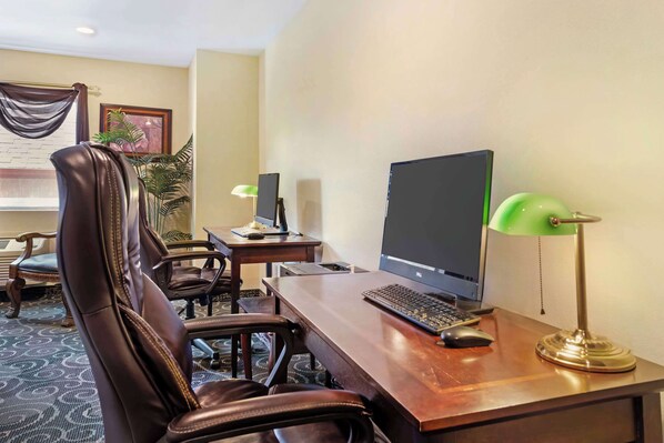 A hotel room with a wooden desk, a computer, two chairs, a lamp, and a plant.