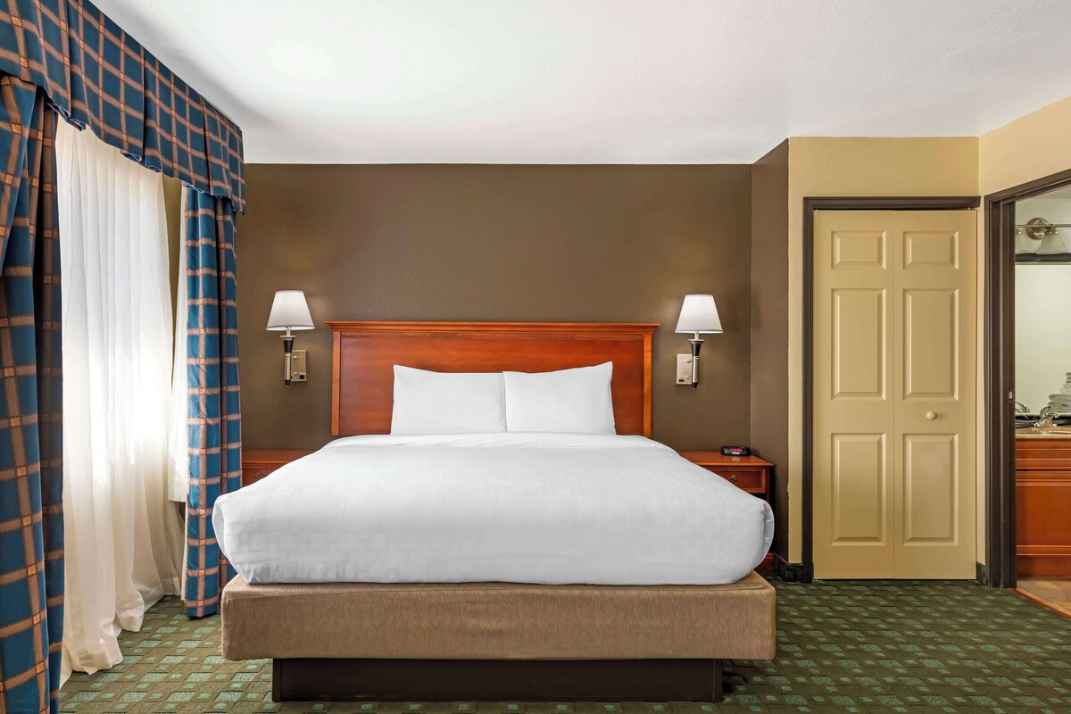 A hotel room with a large bed, two bedside lamps, a wooden headboard, a door, and a mirror.