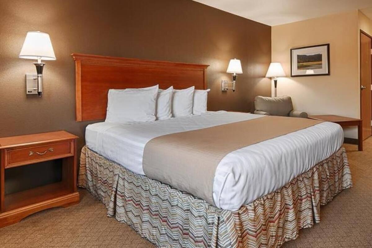 Ein Hotelzimmer mit einem großen Bett, zwei Nachttischlampen, einem Nachttisch, einem Sessel und einem gerahmten Bild an der Wand.