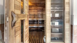A sauna room with wooden slats on the ceiling and walls, a bench, and a glass door.