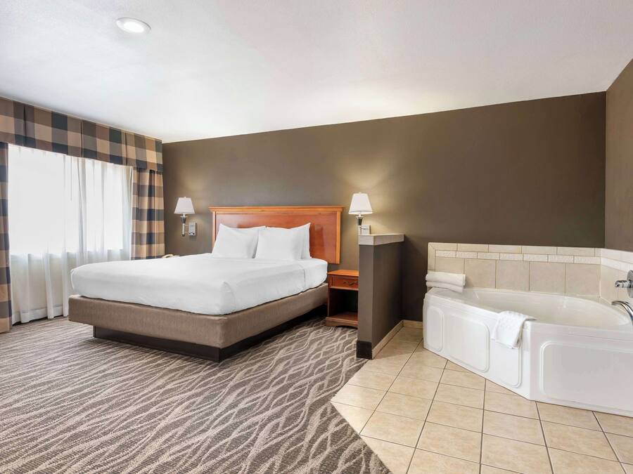 Une chambre d’hôtel avec un grand lit, une salle de bain séparée avec une baignoire et un rideau à carreaux à la fenêtre.