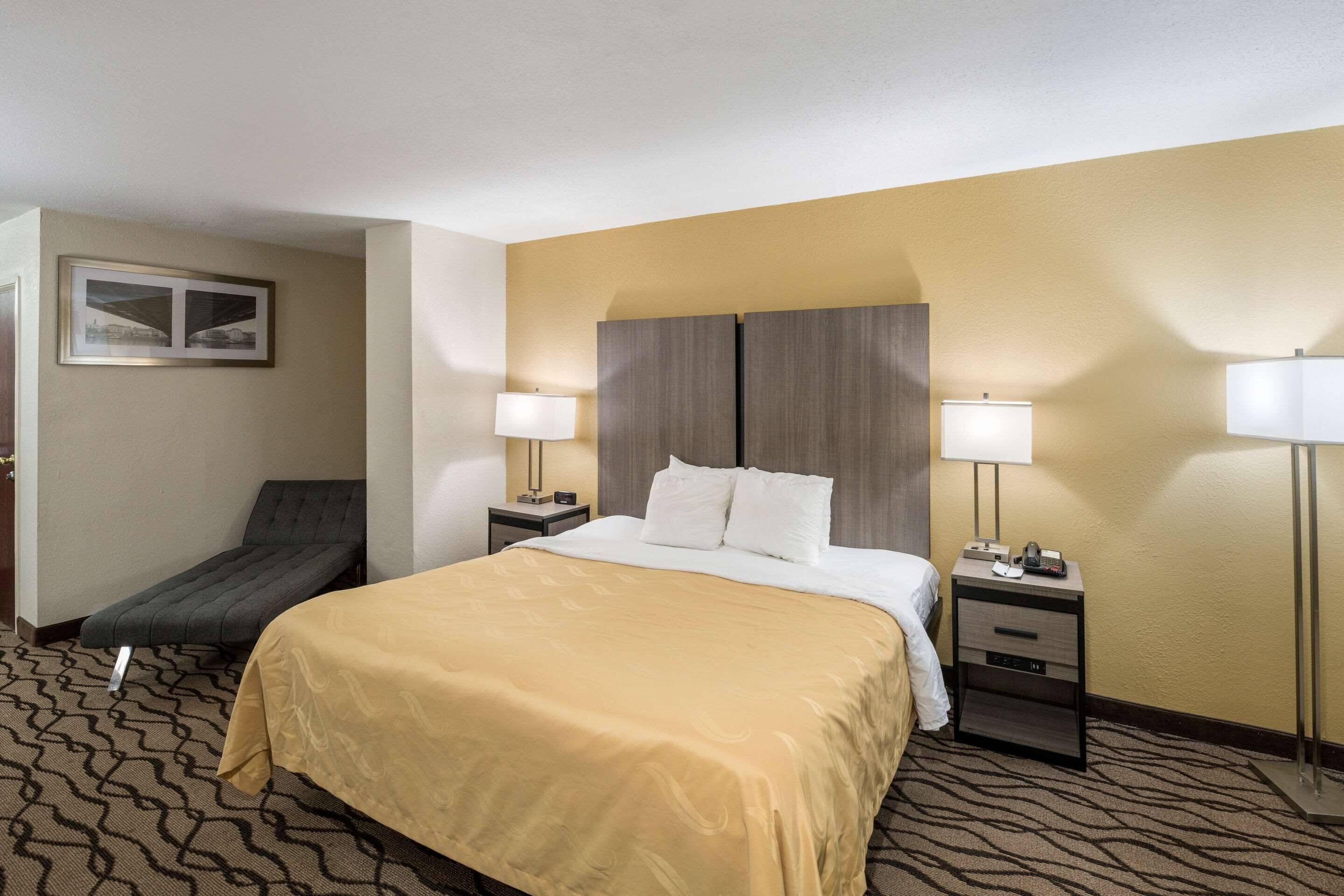 Une chambre d’hôtel avec un lit, deux tables de chevet, un bureau, une chaise et un tableau au mur.