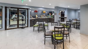 A modern restaurant with a bar area, multiple tables and chairs, and a view of the street through glass doors.