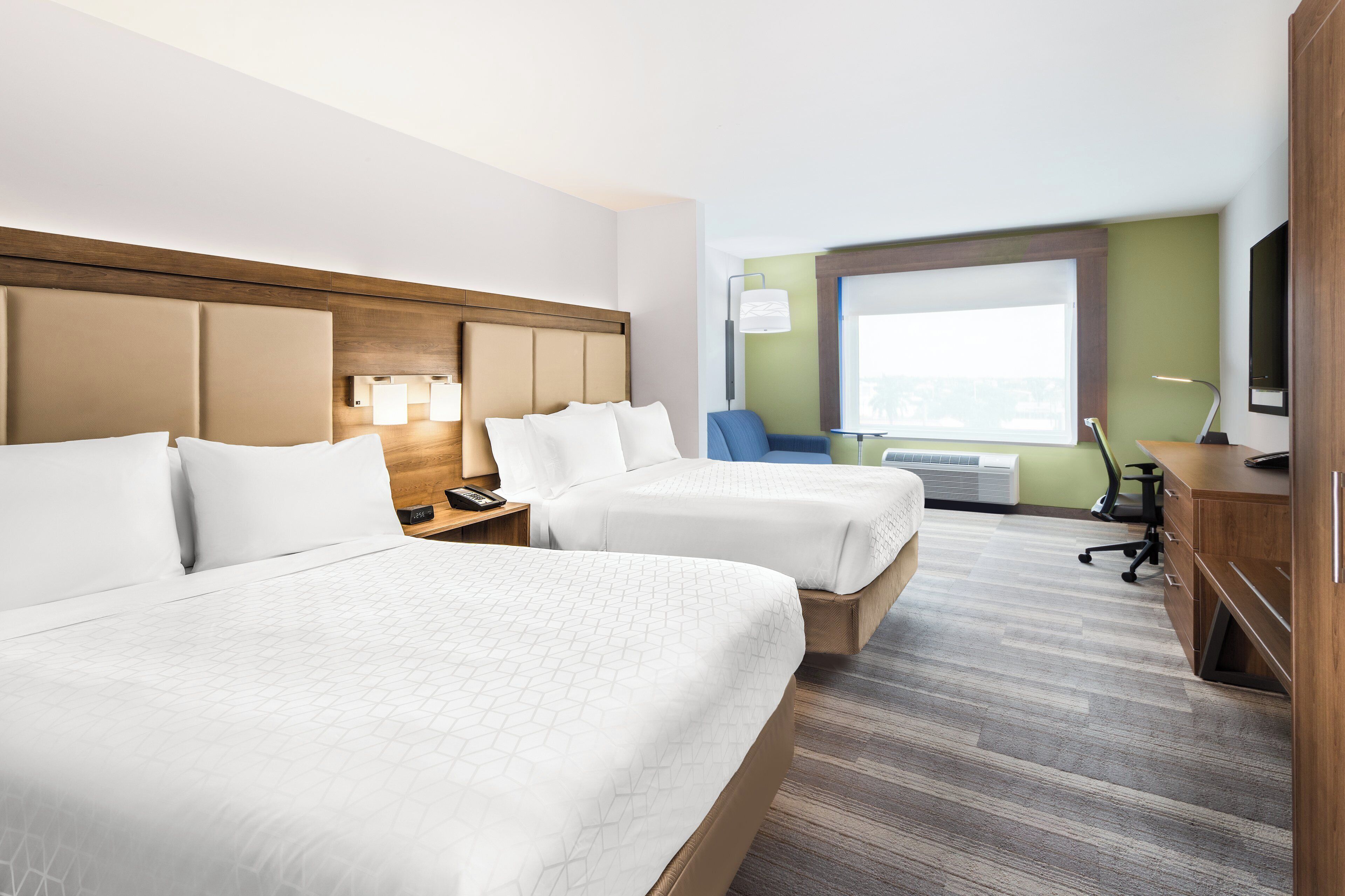 Una habitación de hotel con dos camas, un escritorio, una silla, un televisor y una ventana.