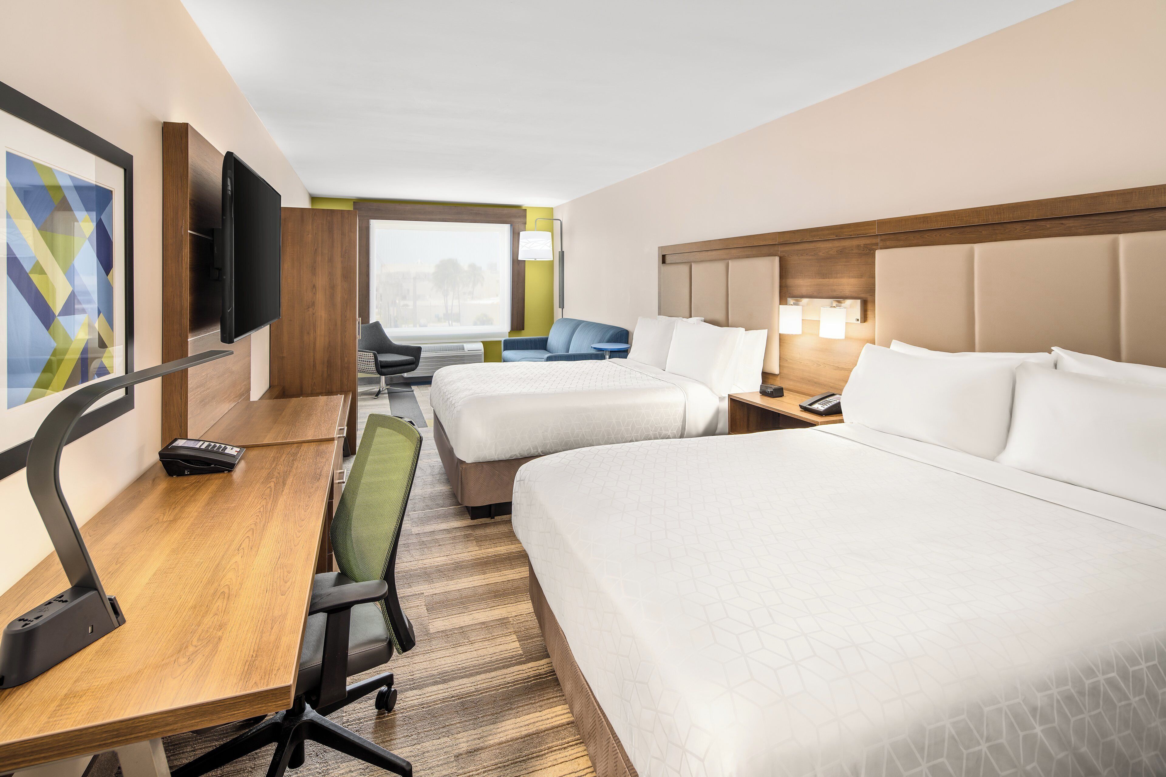 Ett hotellrum med två sängar, ett skrivbord, en stol, en TV och ett fönster med utsikt.