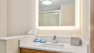 A modern bathroom with a large mirror, a white sink, and a glass shower enclosure.