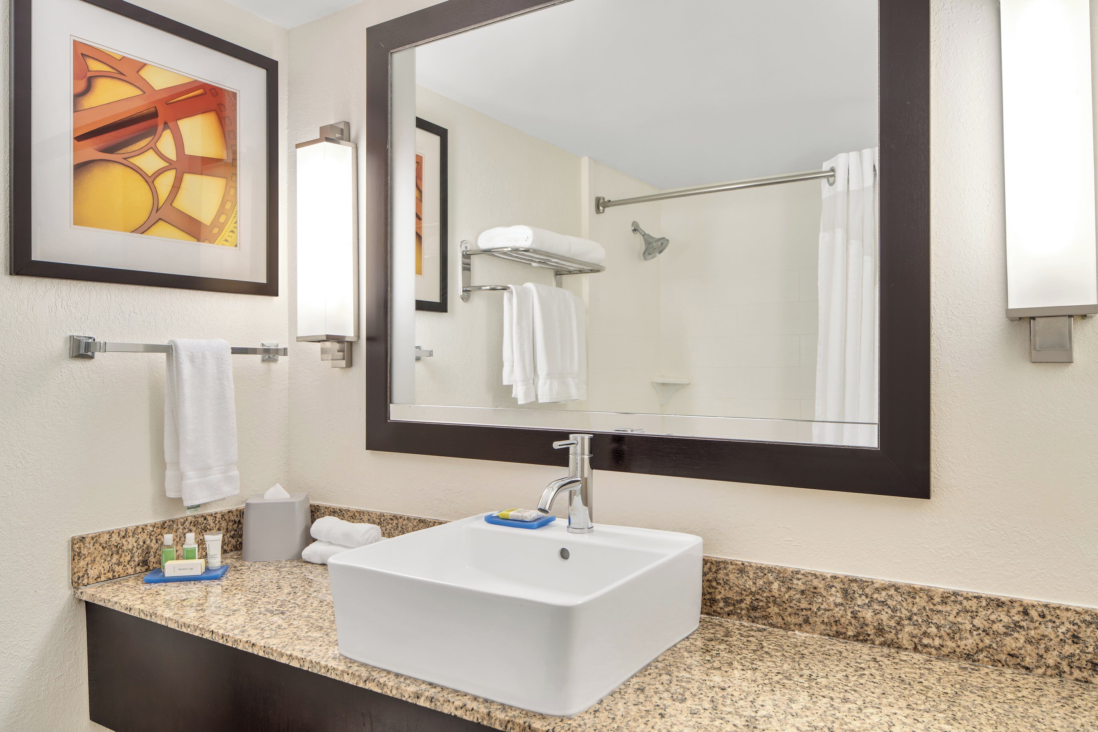 A hotel bathroom with a large mirror, a sink, and a shower.