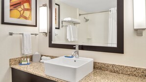 Een badkamer met een wit wastafel, granieten aanrechtblad en een grote spiegel. Handdoeken en toiletartikelen liggen op het aanrecht.