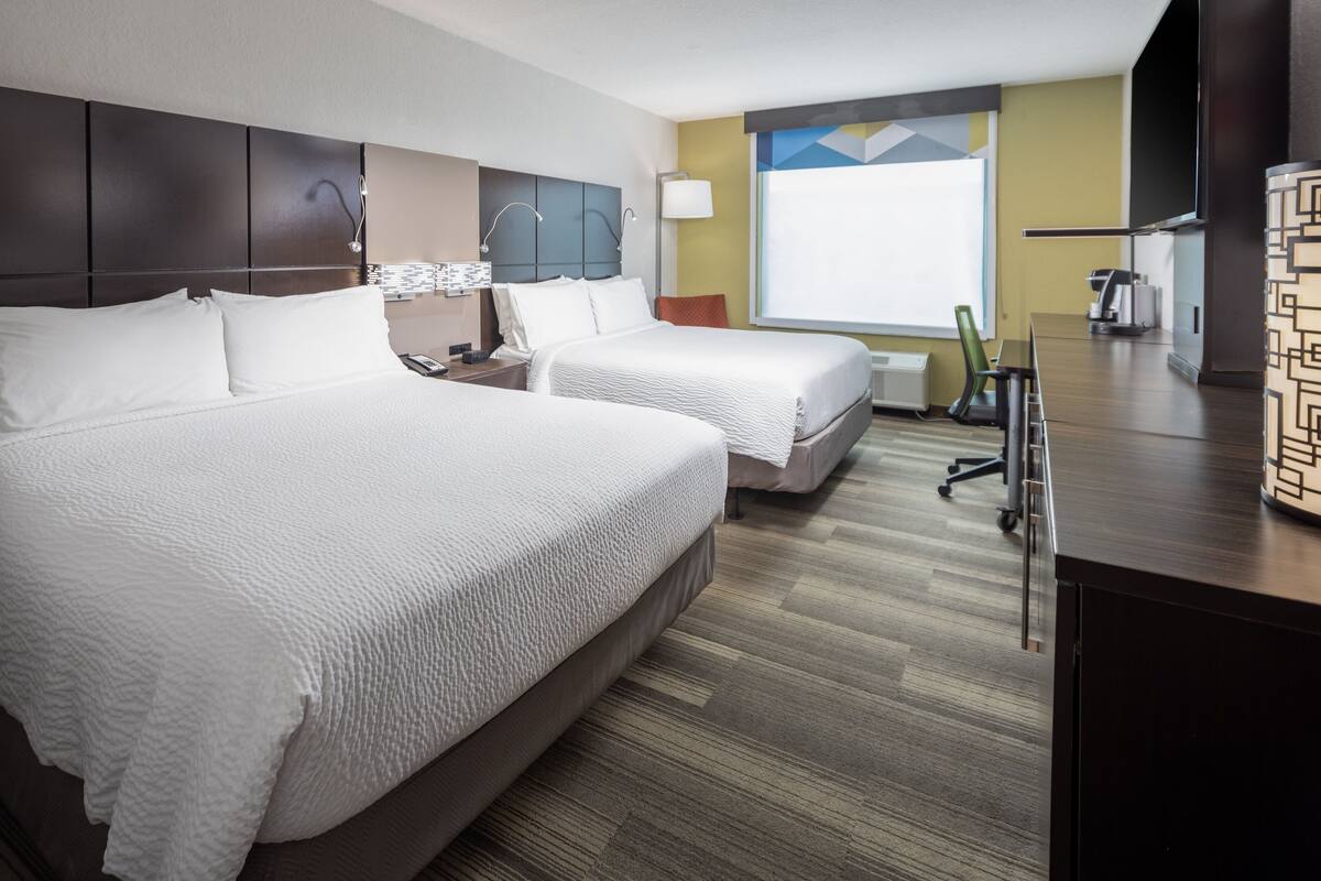 Une chambre d’hôtel avec deux lits, un bureau, une chaise, une télévision et une fenêtre donnant sur un paysage agréable.