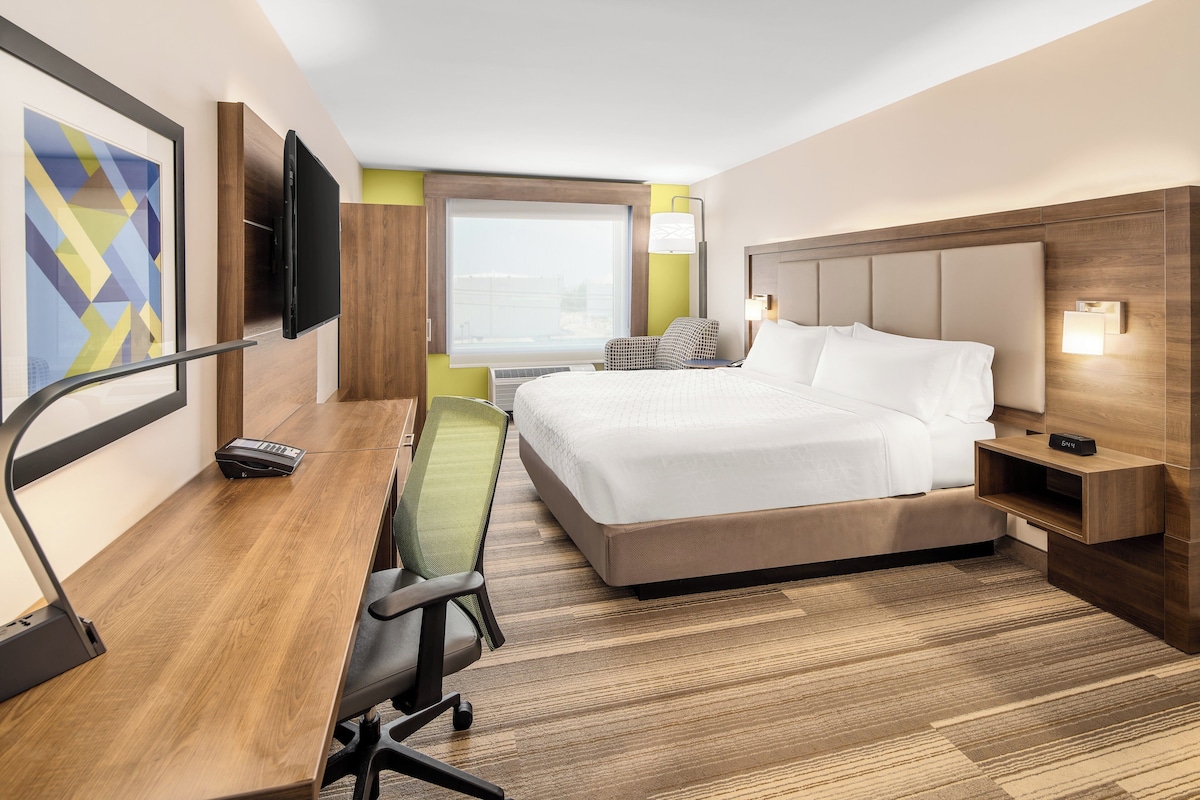 A hotel room with a bed, desk, chair, TV, and a window.