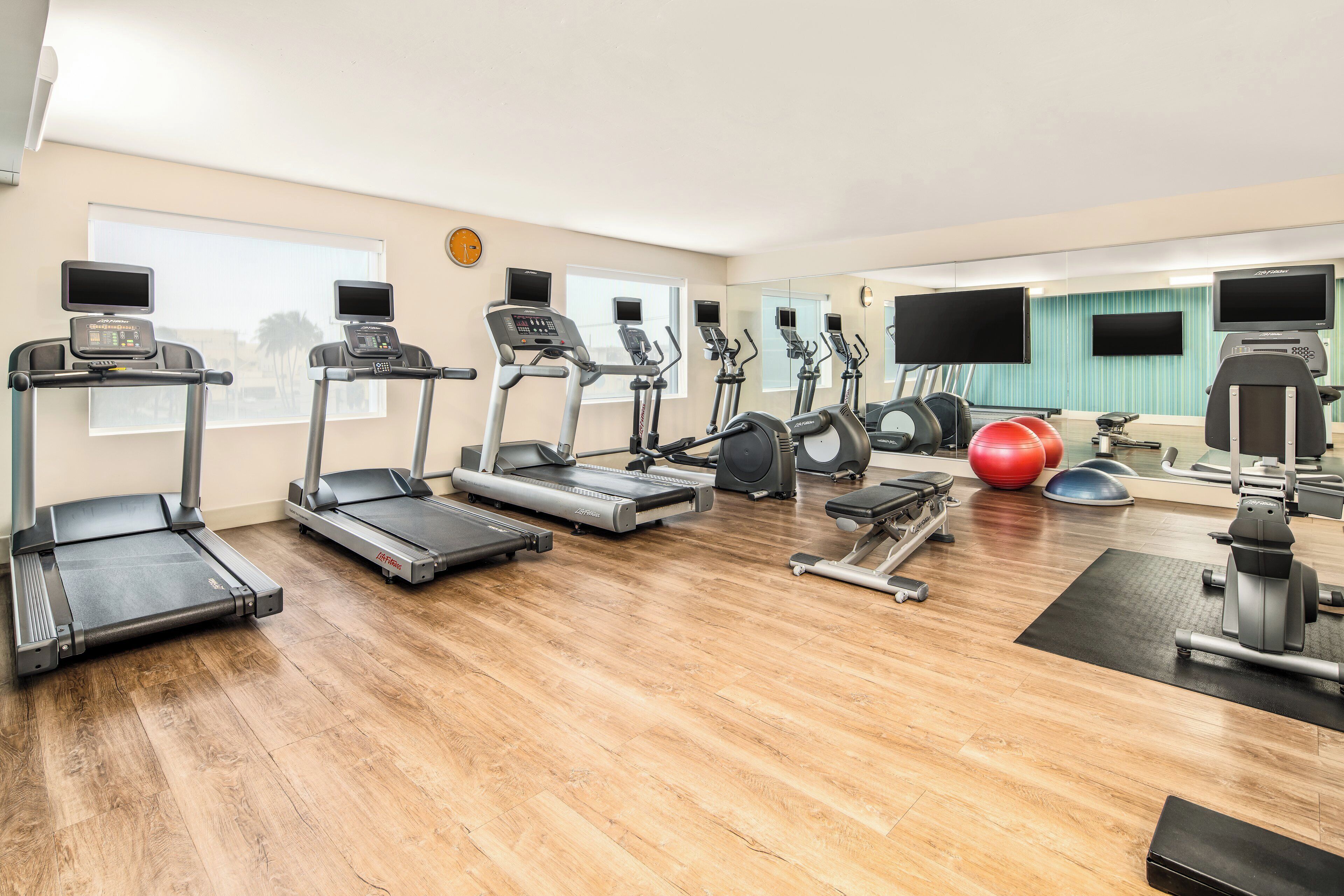 A gym with multiple treadmills, elliptical machines, and exercise balls.