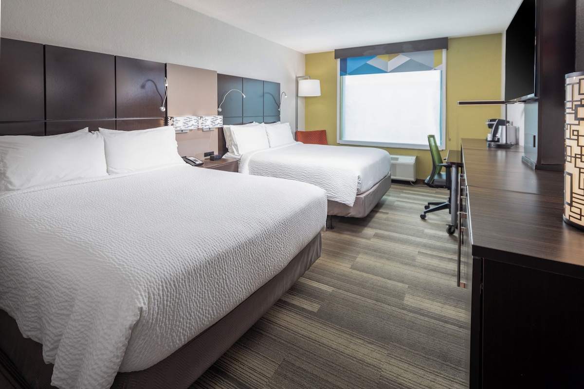 A hotel room with two beds, a desk, a chair, a TV, and a window with a view.