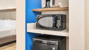 Een hotelkamer met een bed, koffiezetapparaat, magnetron en een minibar op een plank.