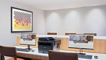 Un salón de conferencias con una larga mesa, dos monitores, una impresora y una obra de arte enmarcada en la pared.