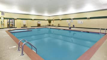 A large indoor swimming pool with a lifeguard chair, pool rules signs, and a pool lift.