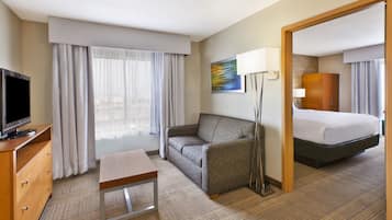 A hotel room with a bed, a sofa, a television, a desk, and a lamp.