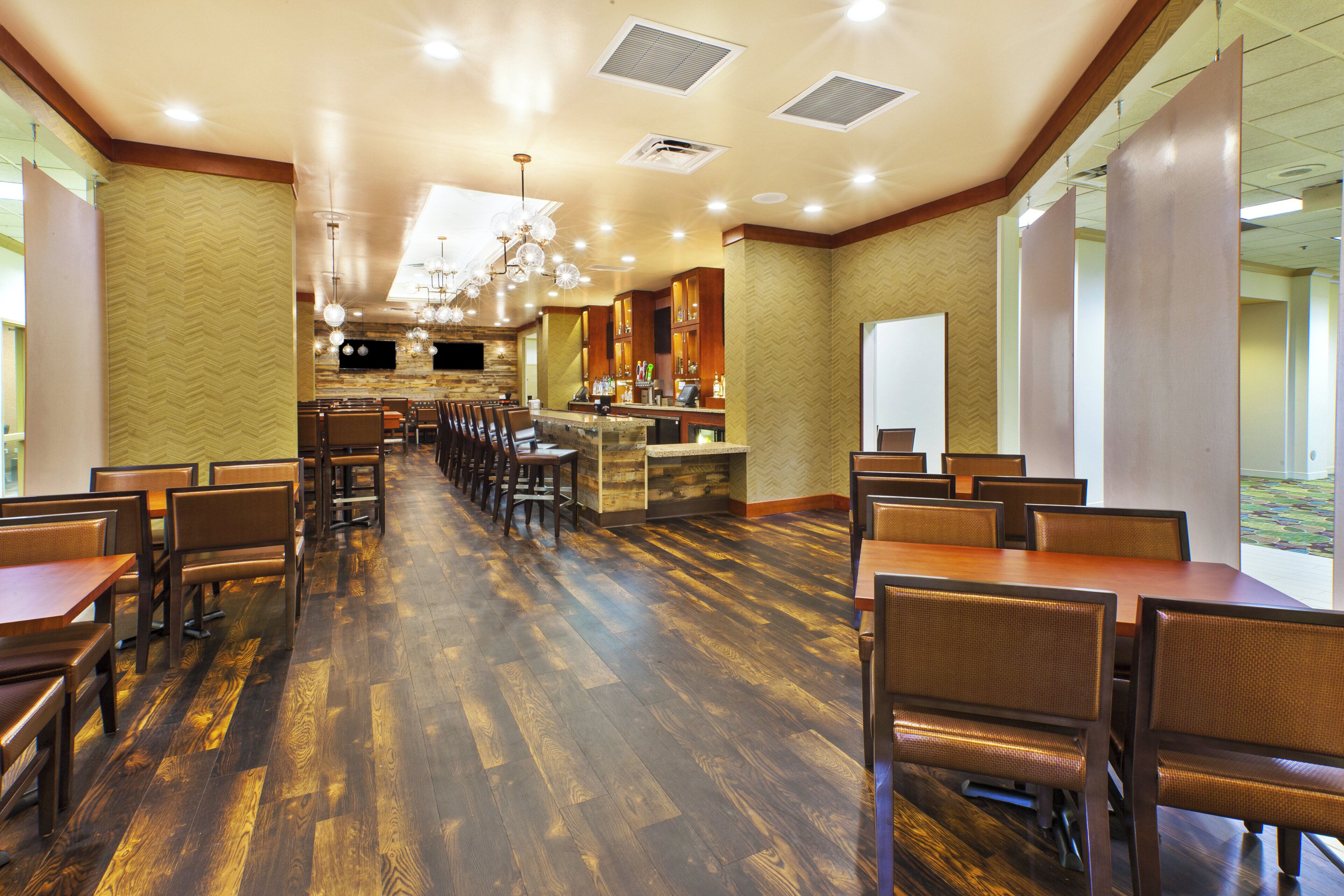A spacious dining area with multiple tables and chairs, a bar counter, and a large window providing natural light.