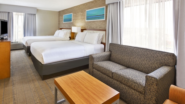 A hotel room with two beds, a sofa, a TV, and a desk.