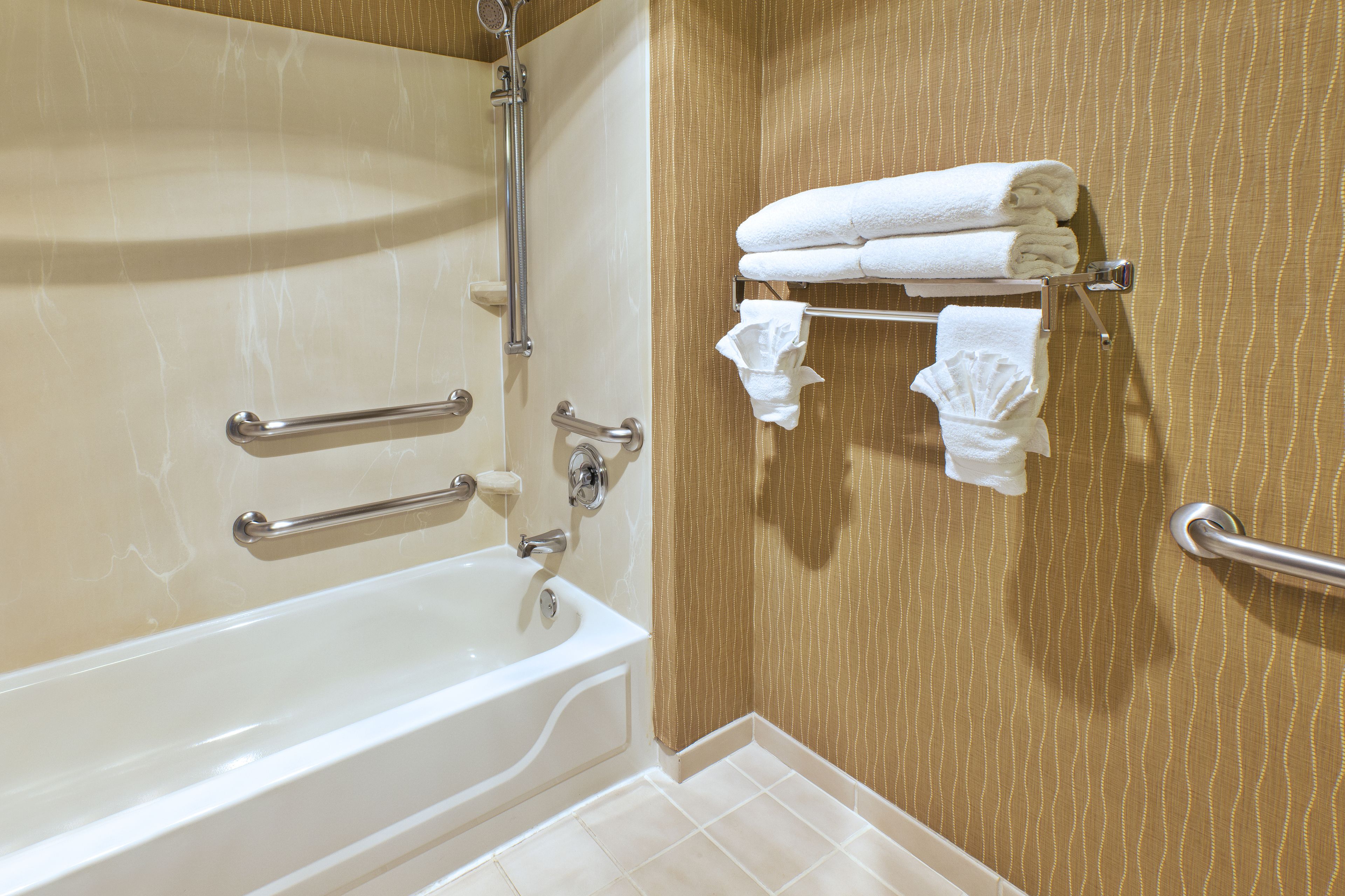 A bathroom with a bathtub, grab bars, and a towel rack with folded towels.