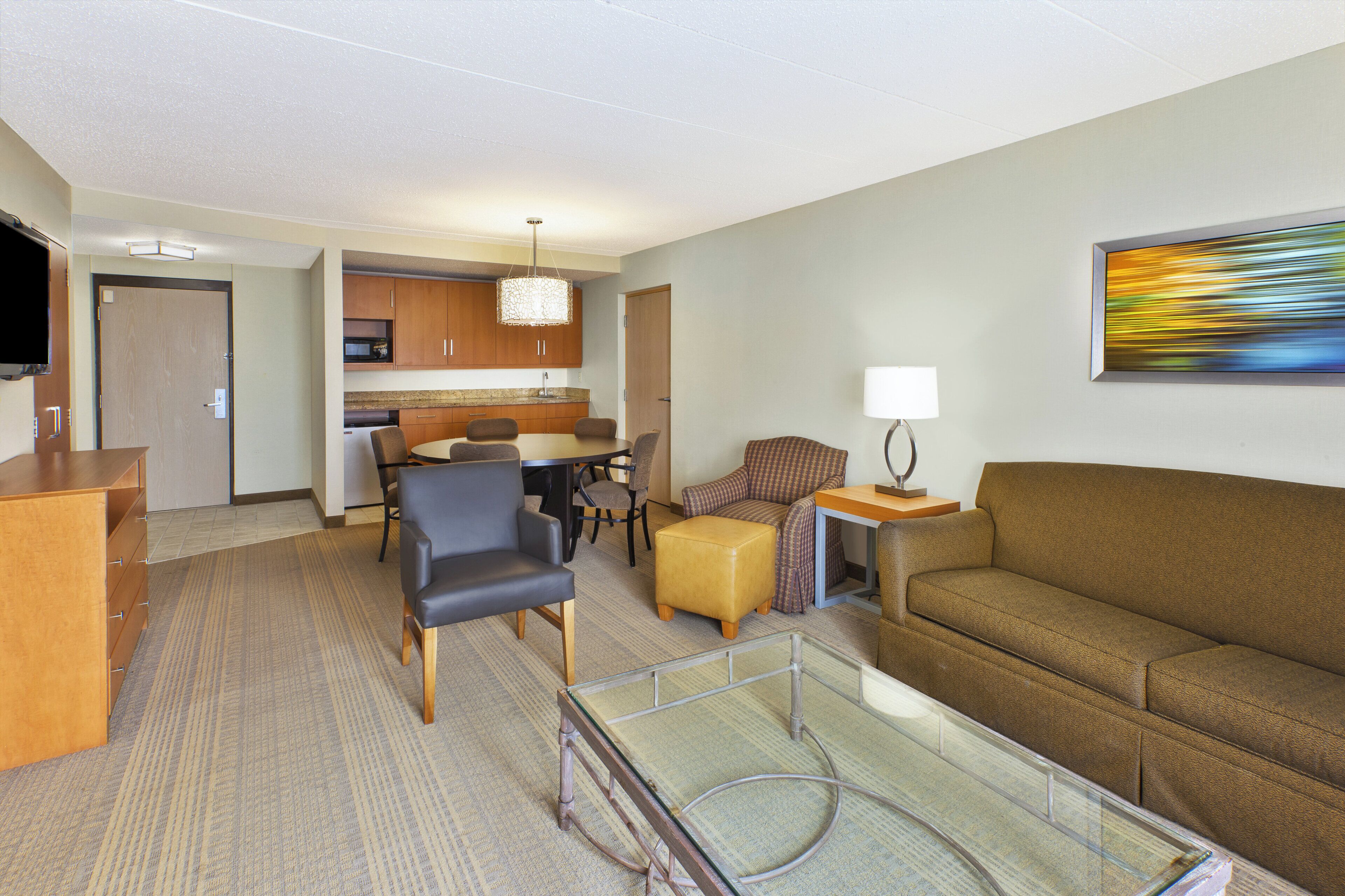 Une chambre d’hôtel comprenant un coin salon, une table à manger avec des chaises, un canapé, une table basse en verre et un téléviseur.