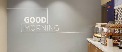 A breakfast counter with a 'GOOD MORNING' sign, a display case with pastries, and a wall-mounted sign.