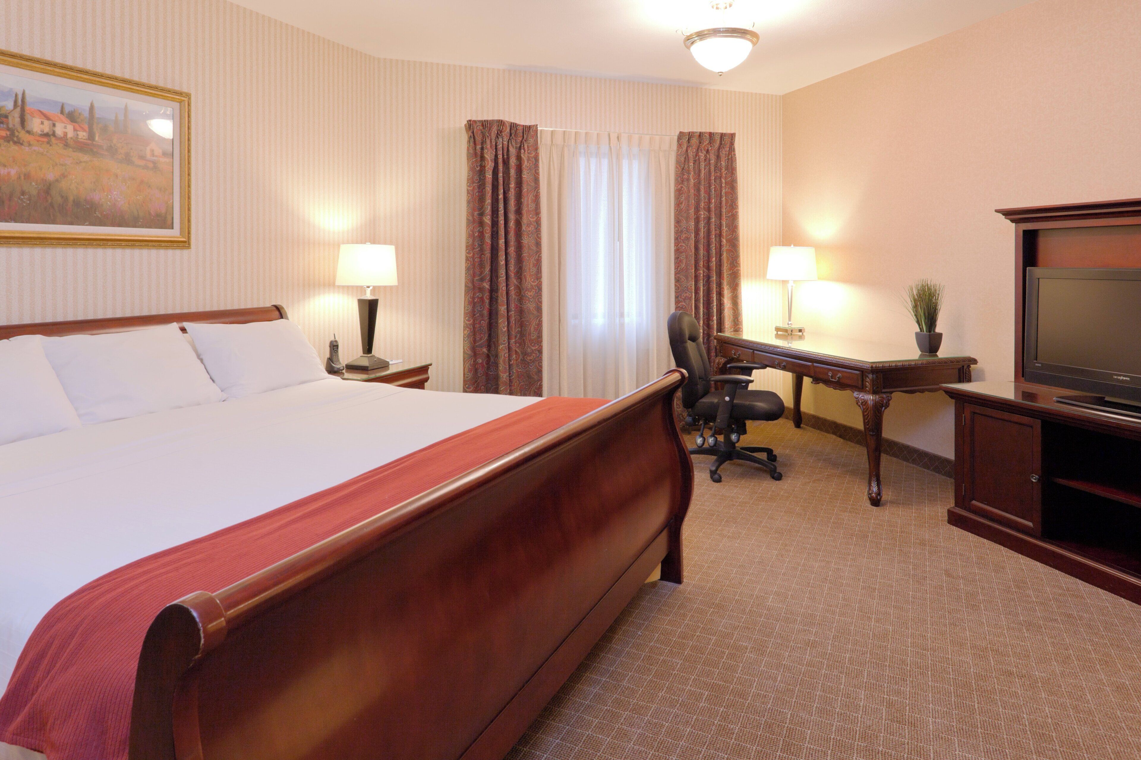 A hotel room with a large bed, a desk with a chair, a television, and a lamp.
