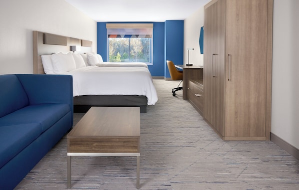 Quarto de hotel com cama, sofá azul, escrivaninha de madeira e guarda-roupa.