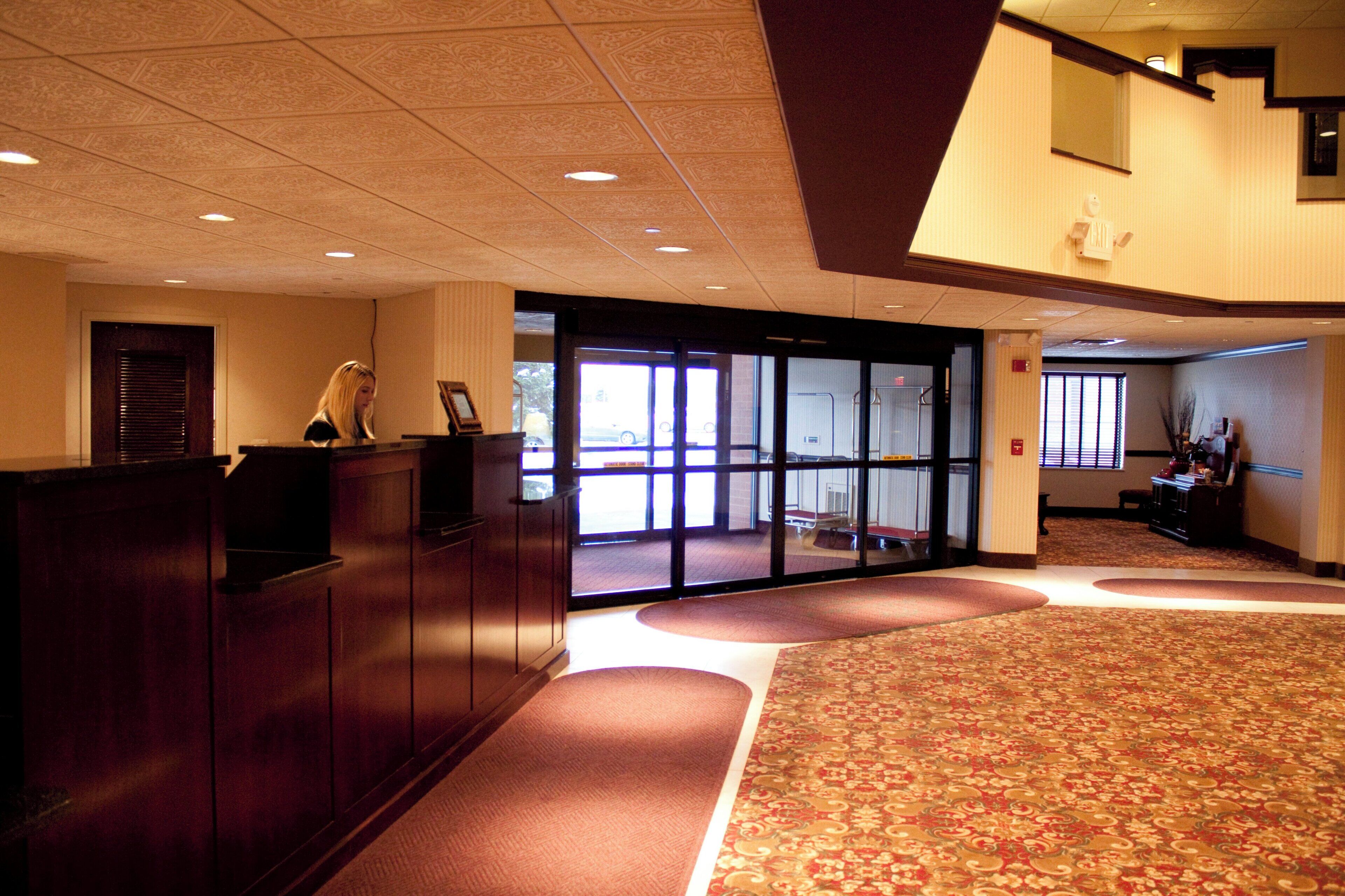 A hotel lobby with a reception desk, a patterned carpet, and a large window with a view.