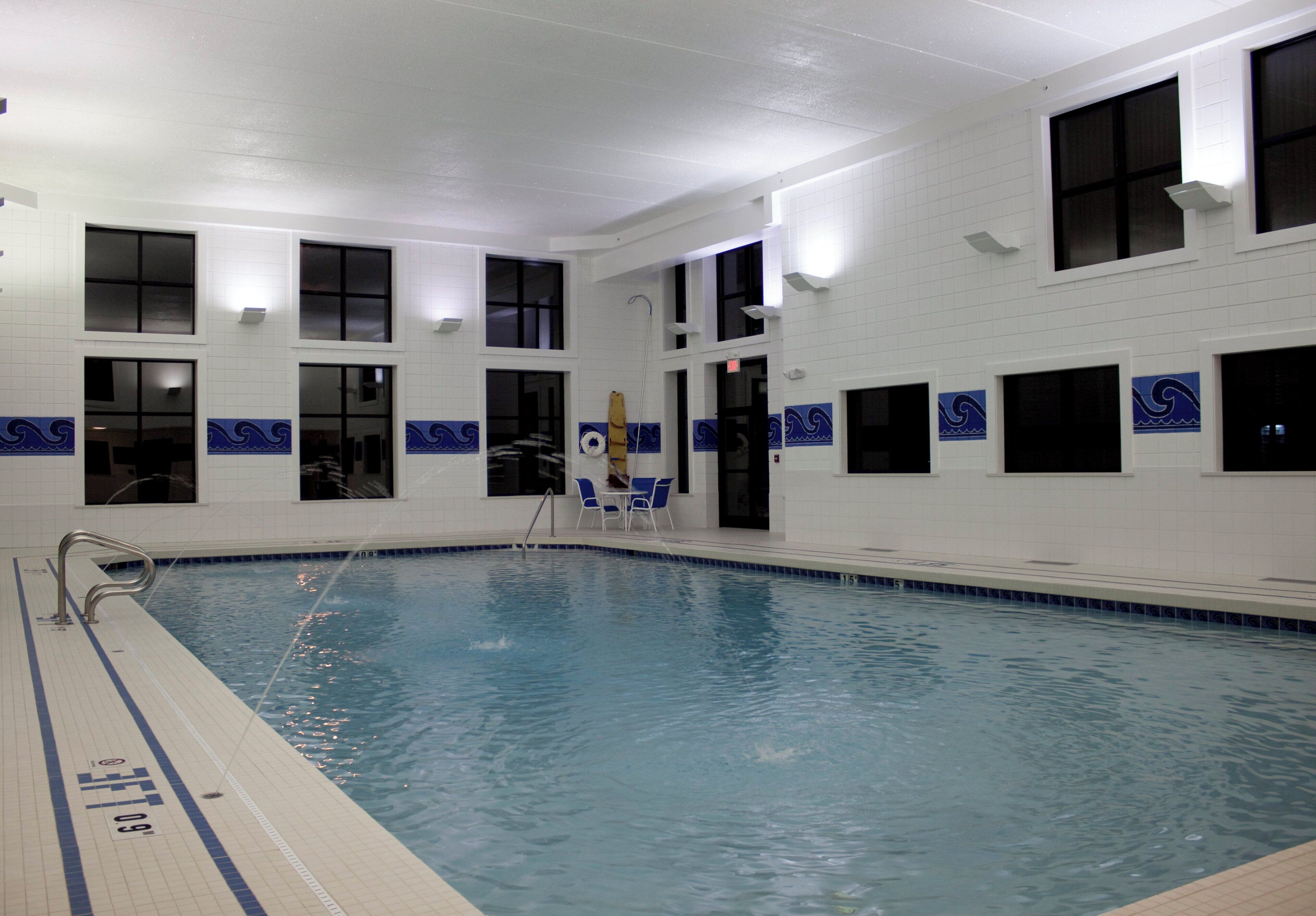 An indoor swimming pool with clear water, tiled walls, and windows.