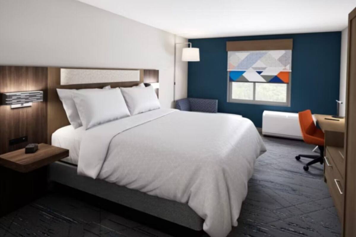 A modern hotel room with a large bed, a desk, and a chair.