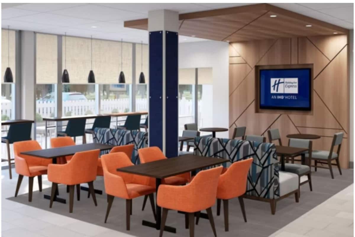 A hotel lobby with seating areas, a large screen displaying the hotel name, and a view of the cityscape through large windows.
