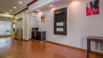 A hotel lobby with a wooden floor, a reception desk, a flat-screen TV, and a wall-mounted artwork.