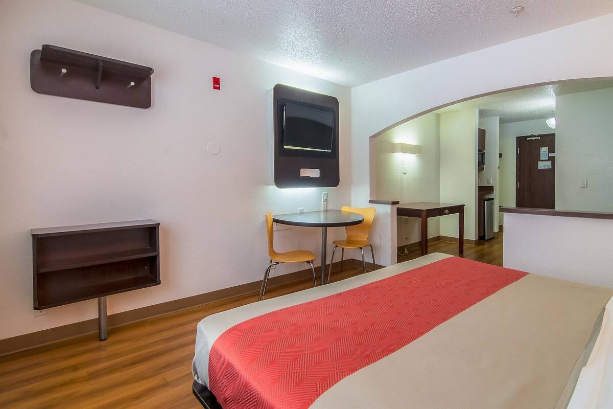 A hotel room with a bed, a desk, a chair, a TV, and a mirror.