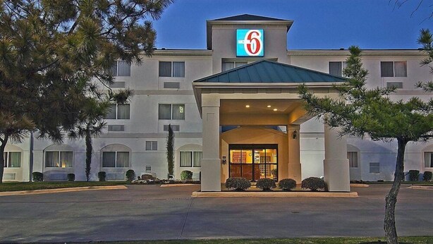 Un motel reconnaissable à son grand panneau indiquant le chiffre « 6 », à son entrée abritée et à son parking.