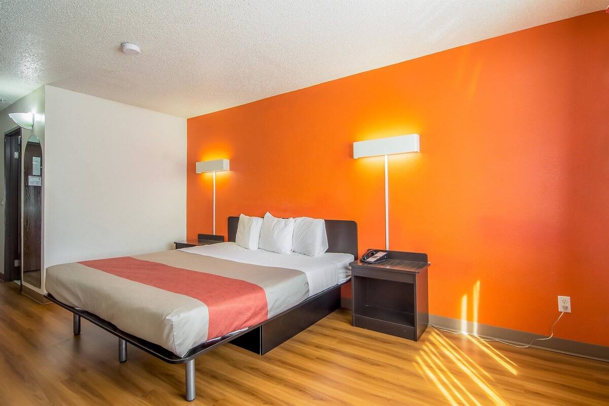 A hotel room with a bed, bedside tables, and two wall-mounted lamps.